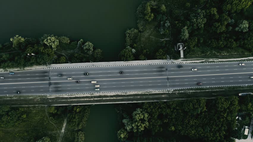 Cars moving along the highway next to a river with trees on both sides, aerial flying drone high view