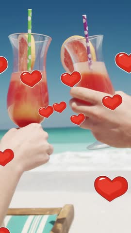 Vertical video: Couple lifting drinks to toast on beach, hearts floating over glasses for travel. Cocktail, grapefruit, polkadot, tropical, vibrant, sunlit, vertical video