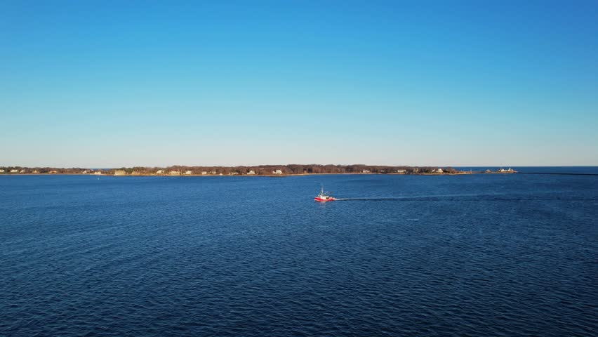 Aerial sunrise view of fishing boat crossing calm blue waters near Gloucester, Massachusetts. Scenic New England coastline with maritime industry, open ocean horizon and peaceful harbor atmosphere.