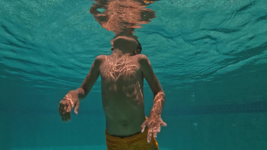Cute Kid Dives in the blue water Pool.