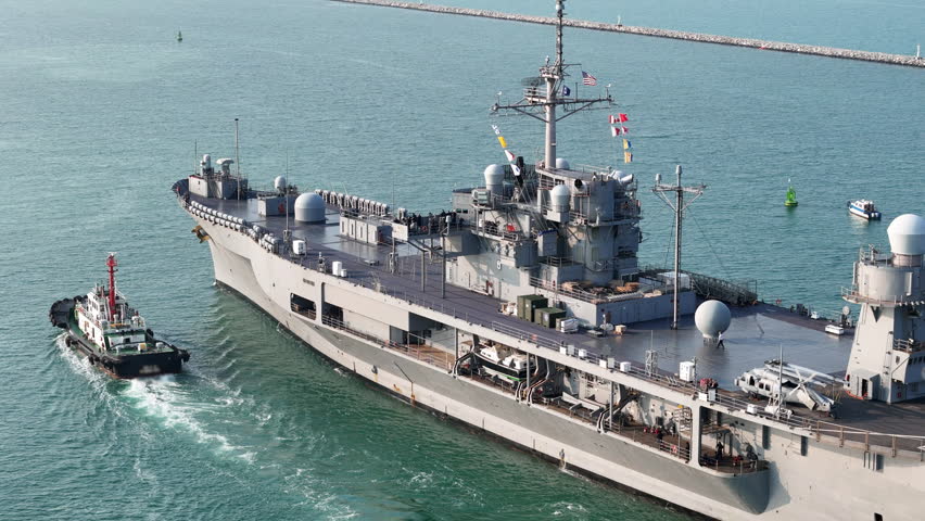 large naval amphibious assault ship being assisted by tugboats in the strategic Strait of Hormuz. Concept of maritime security, naval power projection, and protection of international shipping lanes.