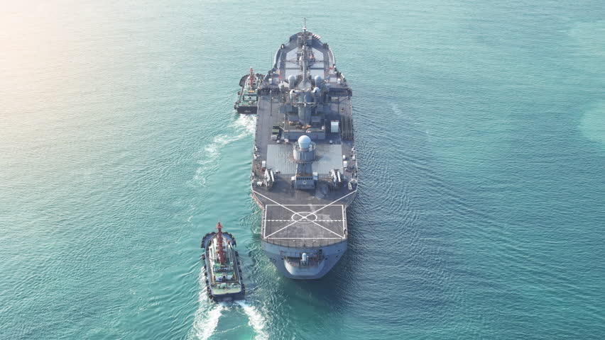 large naval amphibious assault ship being assisted by tugboats in the strategic Strait of Hormuz. Concept of maritime security, naval power projection, and protection of international shipping lanes.