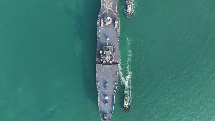 large naval amphibious assault ship being assisted by tugboats in the strategic Strait of Hormuz. Concept of maritime security, naval power projection, and protection of international shipping lanes.