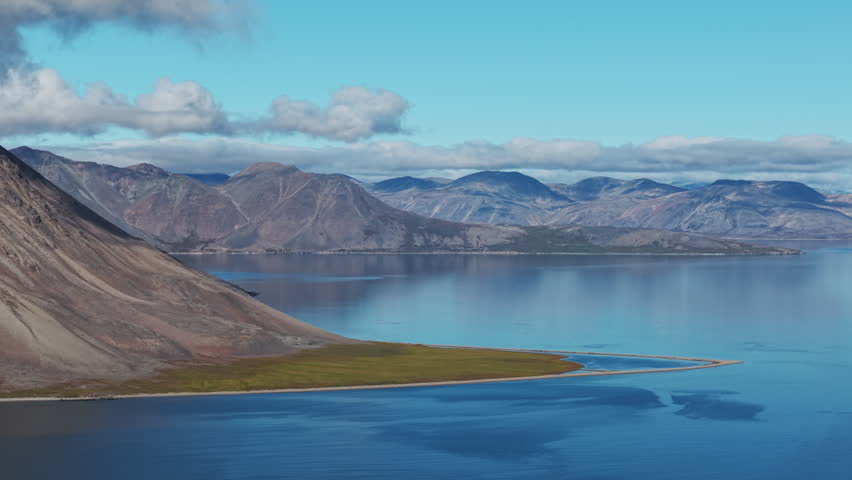 Aerial view of Rumilet Bay in Chukotka with turquoise water and tundra shore. Slow pan reveals a volcanic mountain and distant ranges. Early autumn late evening scene for remote travel and exploration