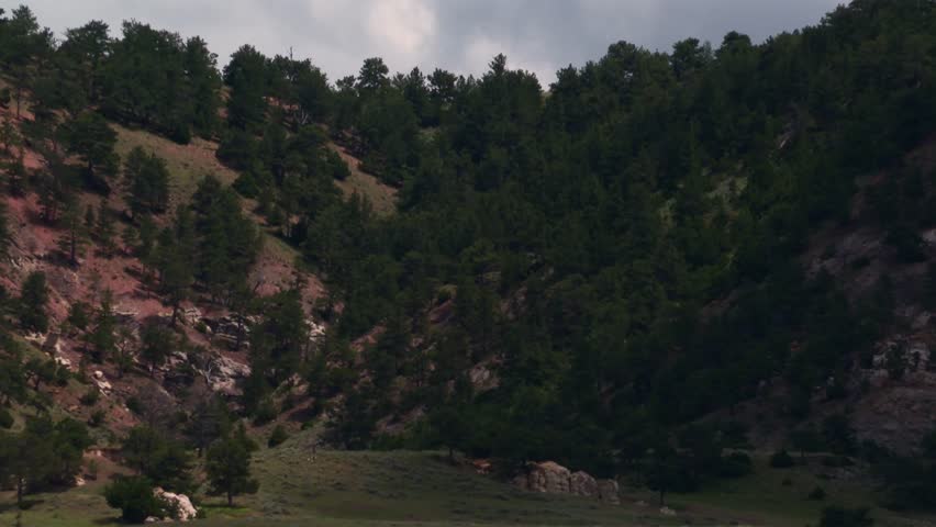 Nebraska badlands landscape featuring hills, green pastures, and cloudy sky in zoom out shot