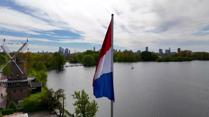 Aerial view of a traditional windmill by a lake with a city background.