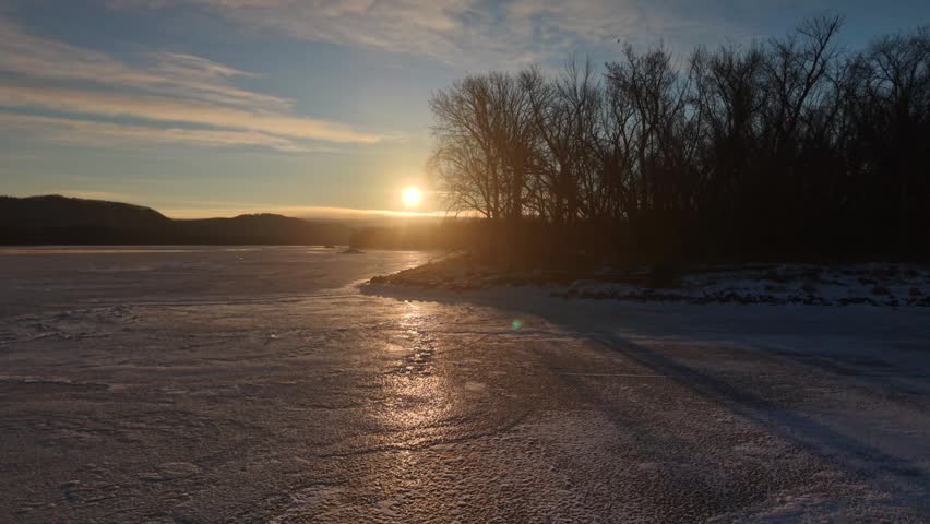 A serene winter sunset casts shadows over an icy lake and barren trees, A serene winter sunset view over frozen trees.