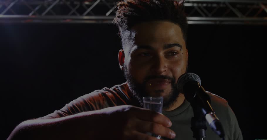 Man lifting glass drinking raising arm cheering on truss with mic and animated confetti around him. Performer, singer, stage, theater, stand, spotlight, lighting