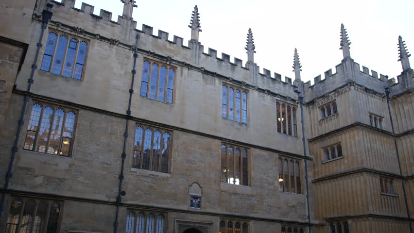 Building courtyard at Oxford University with Gothic stone walls, tall windows, and spired roofline, captured in a wide view showcasing historic college architecture and symmetry
