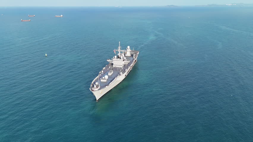 large naval amphibious assault ship being assisted by tugboats in the strategic Strait of Hormuz. Concept of maritime security, naval power projection, and protection of international shipping lanes.