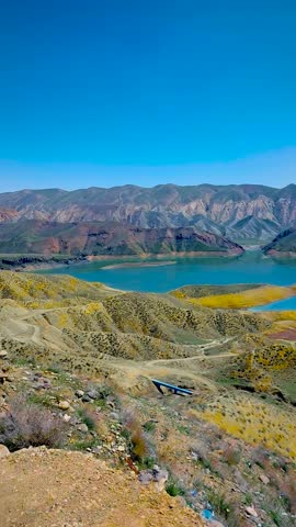 Vertical panoramic shot of the turquoise Azat Reservoir surrounded by colorful Yeranos mountains under a clear blue sky in Armenia.