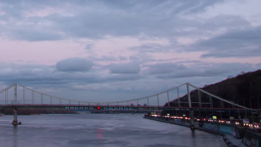 Timelapse of a large bridge over a river in central Kyiv, Ukraine, as the city sunsets on a rainy day