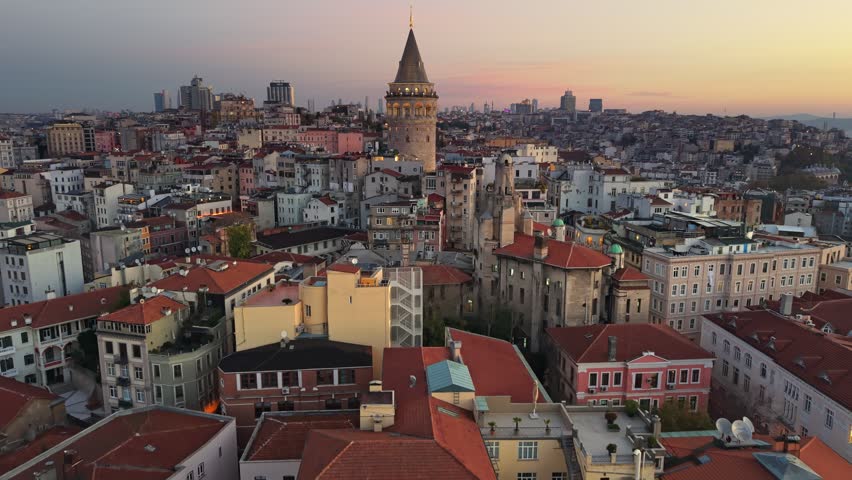 Breathtaking aerial view of the historic Galata Tower before sunrise, city lights of Istanbul begin to glow under golden sky. Majestic Galata Tower rises above the dense buildings of Istanbul