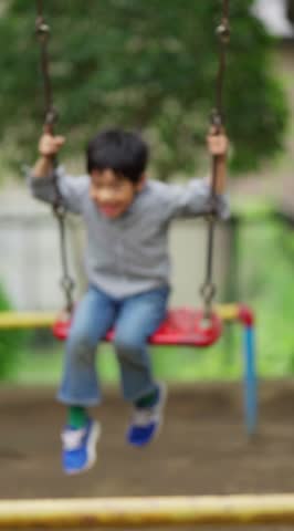 A first-grade boy swinging on a swing - vertical video