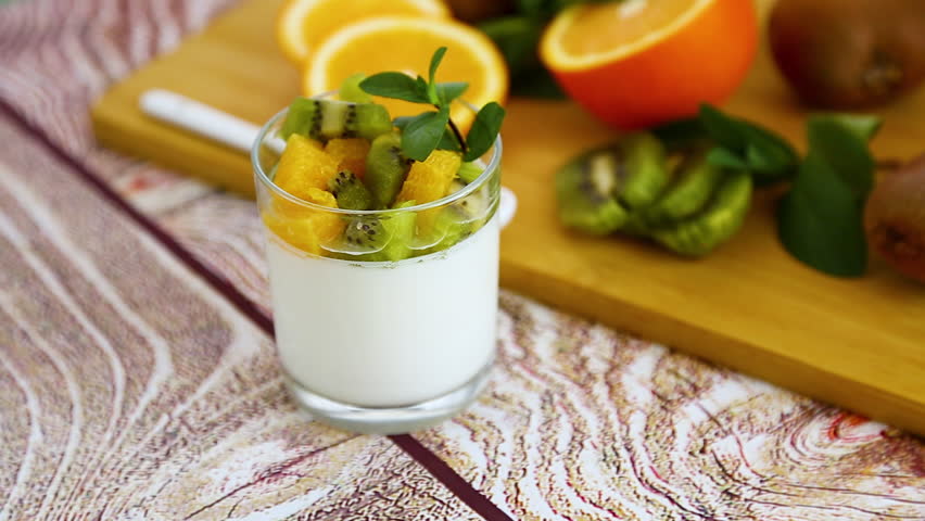 creamy yogurt dessert with kiwi and orange on wooden background