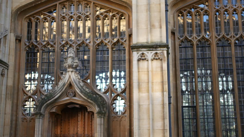 Doorway entrance at Oxford University framed by intricate Gothic stone carvings and leaded glass windows, captured in a close up highlighting texture and historic craftsmanship