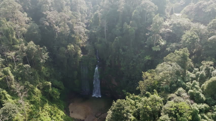 Thác Tiên waterfall wide shot with misty atmosphere and soft sunbeams filtering through the rainforest canopy, Vietnam.