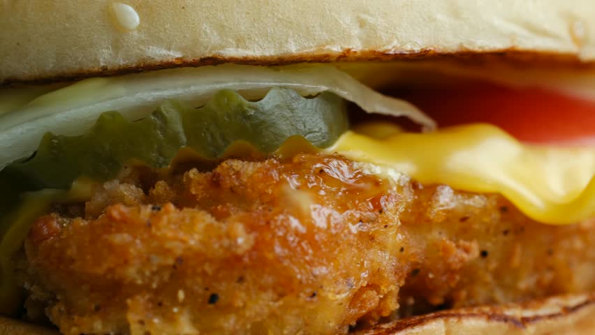 Macro view revealing detailed textures of freshly made crispy chicken burger with melted cheddar cheese, tomato pickles sesame seed bun, showcasing appetizing layers. Delicious burger extreme close up