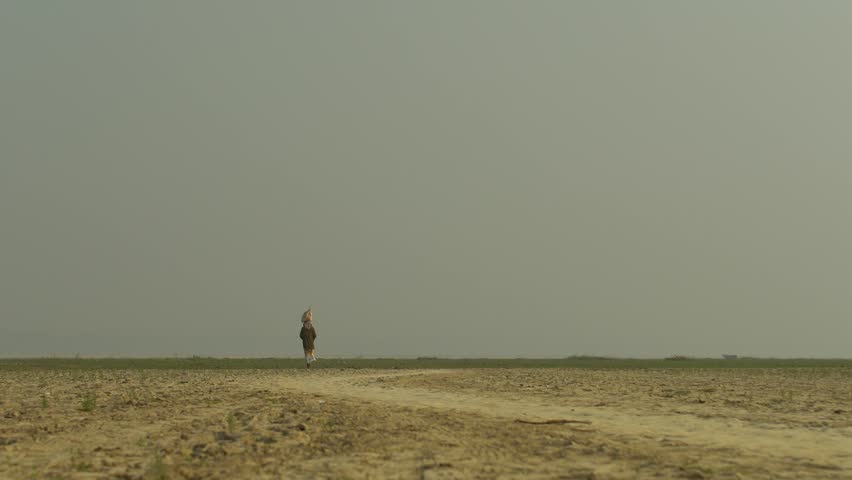 Rural man Walking with Load on Head in Arid Desert Landscape.