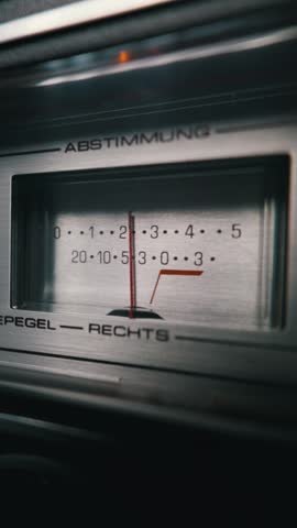 An illuminated analog audio meter displays volume sound levels with a red needle on a brushed metal stereo receiver. Concept of retro music recording, sound engineering, and audio nostalgia.