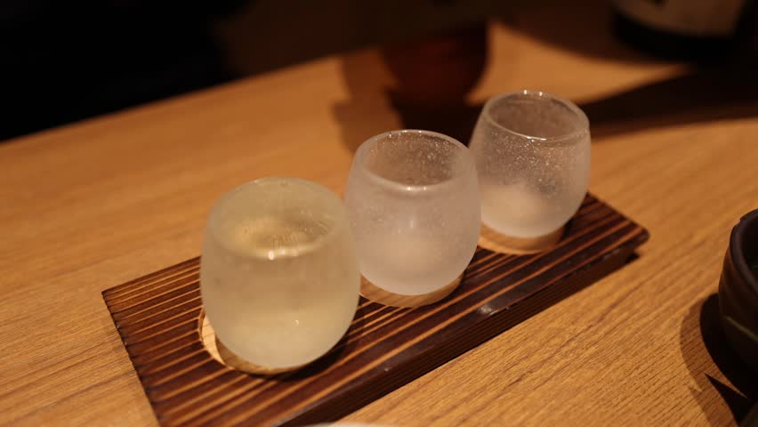 Sake pouring, beverage tasting, small glasses, wooden board.