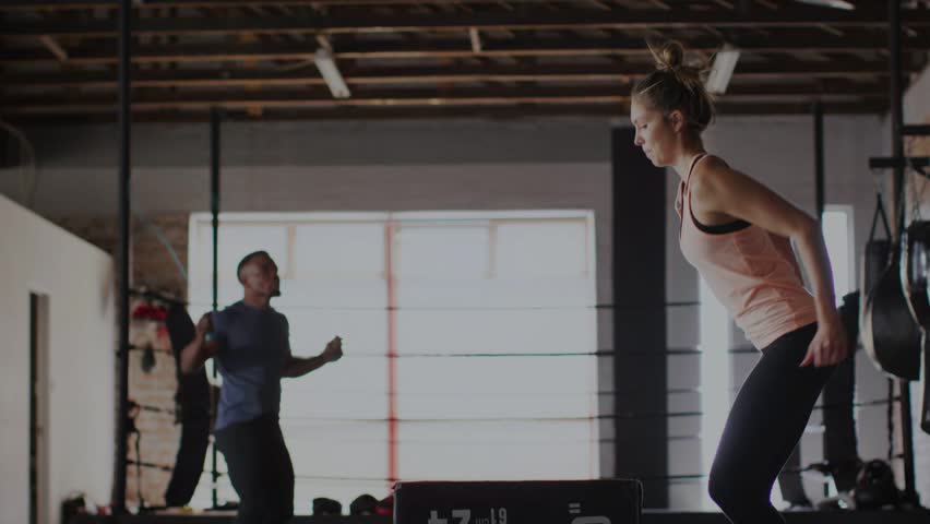 Woman doing repeated plyo box jumps in fitness gym for power, waveform sweeping cueing jump timing. Platform, circuit, cardio, teamwork, athletic, silhouette, backlit