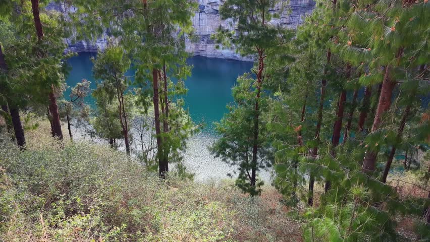 Serene, turquoise lake nestled within a rocky canyon. Tall pine trees frame the view from above, their green foliage contrasting with the deep blue water below