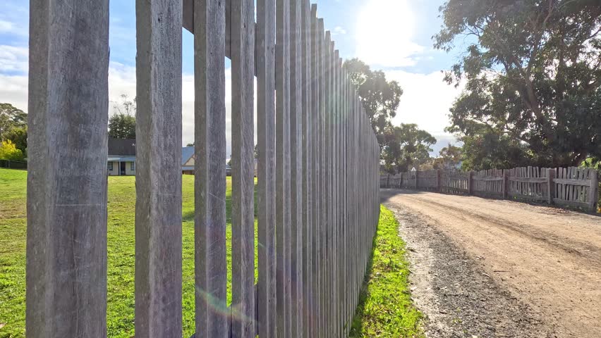 Slow motion video along rustic timber picket fence on sunny day.