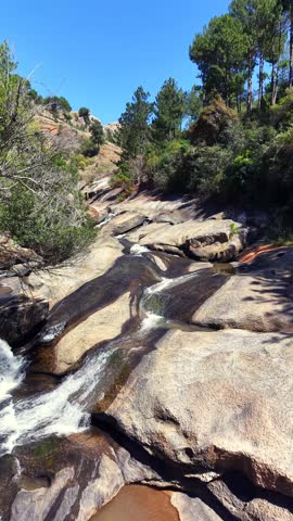 Rushing water flows over sunlit, mossy rocks in a forested canyon. Ancient stone structures hint at forgotten history amid nature