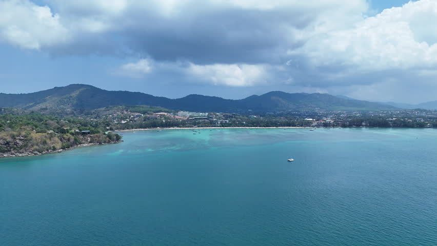 Aerial View of Serene Coastal Landscape with Turquoise Waters, Lush Hills, and Distant Shoreline Under Partly Cloudy Sky