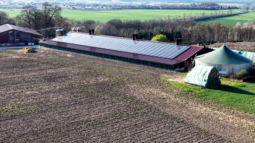 Aerial view of a modern farm featuring a biogas plant and solar panels on the barn roof