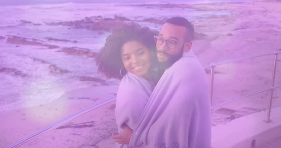 Couple wrapping in blanket by railing, cool breeze pulling hug, purple overlay making travel ad. Seaside, promenade, ocean, wind, warmth, embrace, laughter