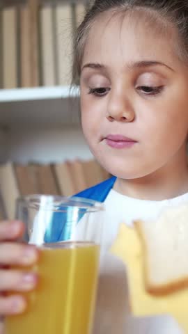 A girl is drinking a glass of orange juice while holding it close to her face. The girl takes a careful sip, enjoying the refreshing orange juice.