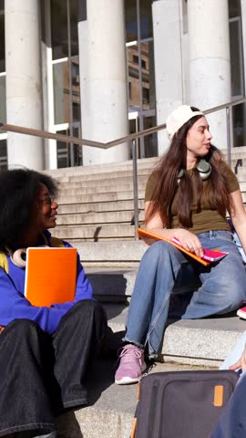 Group of happy young multiracial college students sitting on the steps of the university building, chatting and laughing together during a break between classes on a sunny day