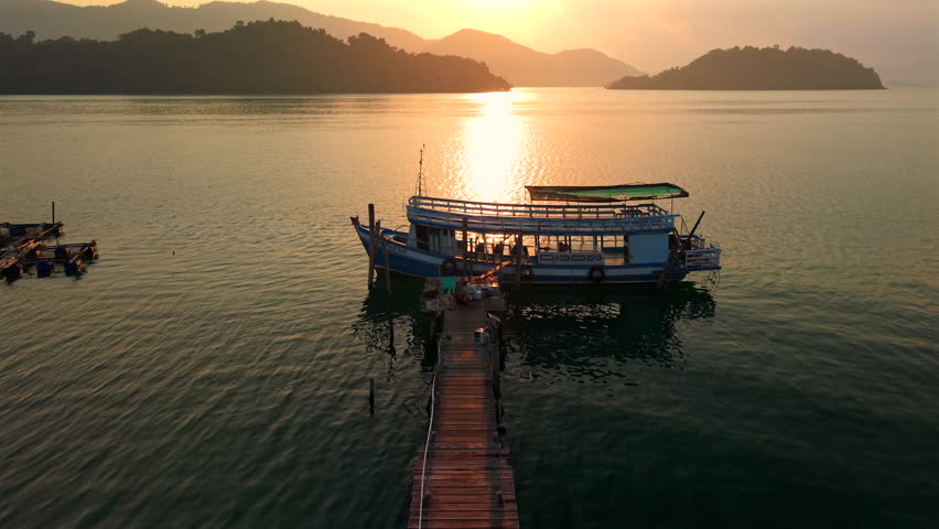 Traditional Thai wooden fishing boat moored at a pier during a golden sunset.