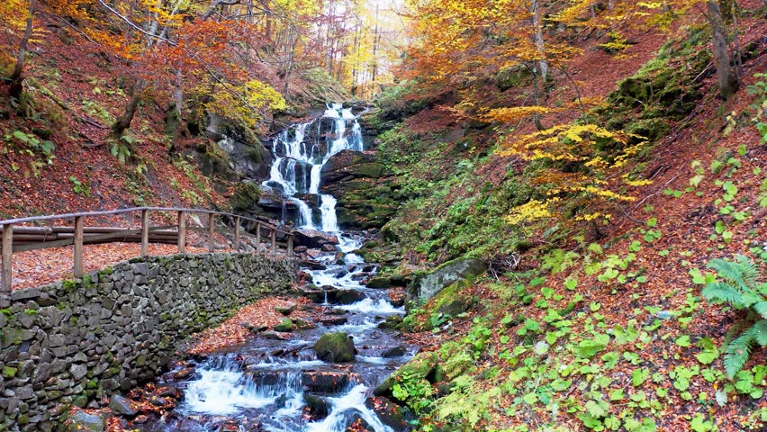 Narrow stream falling down mountain slope in autumn forest