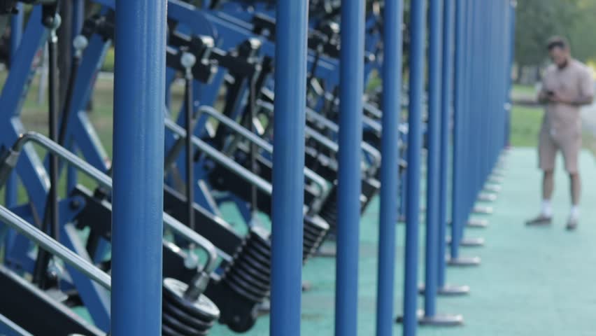 Lineup of blue fitness machines stretches into the distance on a green rubberized surface. The scene conveys a sense of order and readiness for physical activity, inviting passersby to engage in exerc