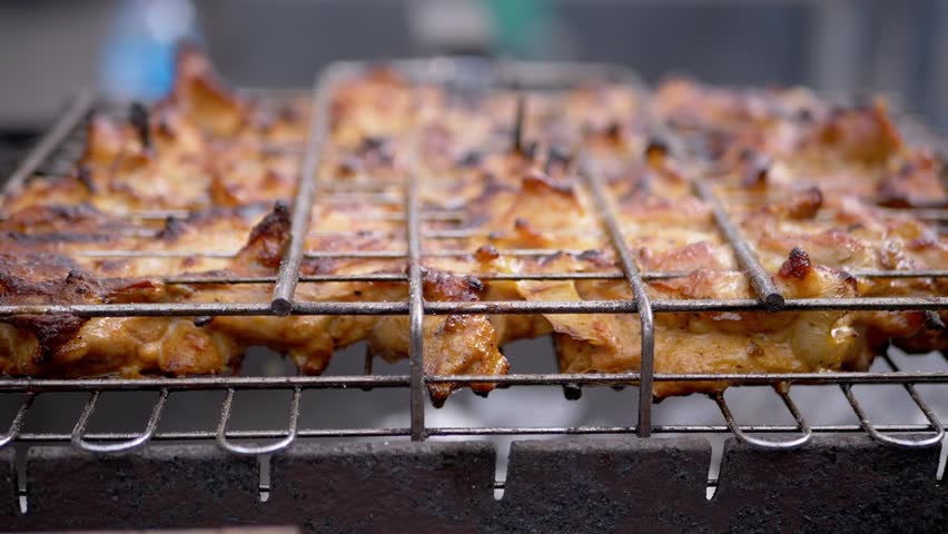 Seasoned chicken pieces grill on a metal wire rack, glistening under warm natural light with a golden brown crust. Concept of outdoor barbecue, summer cooking, and street food preparation.
