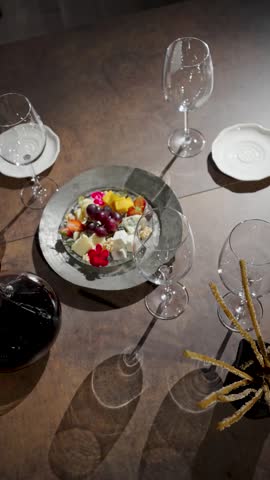 Elegant Wine and Cheese Plate Setting in Luxury Restaurant. Gourmet cheese platter with grapes and strawberries, empty wine glasses, a decanter of red wine, and breadsticks