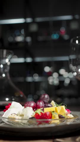 Elegant Wine and Cheese Plate Setting in Luxury Restaurant. Gourmet cheese platter with grapes and strawberries, empty wine glasses, a decanter of red wine, and breadsticks