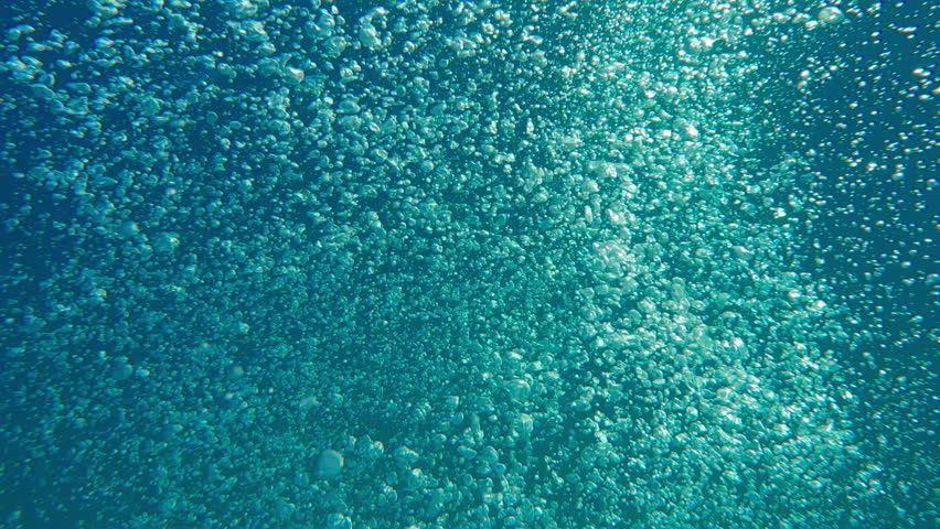Follow shot of vibrant air bubbles from view above to bubbling water surface. Stream of bubbles rushes upwards against blue water to surface of sea. Natural underwater background with air bubbles popping up
