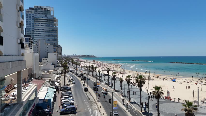 Aerial 4K view of Tel Aviv coastline, bustling promenade, luxury hotels, and sandy beach on a sunny day, Israel