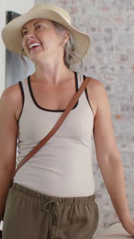 Vertical video: Entering pair touring room, woman in straw hat lifting crossbody bag, man in denim. Couple, visitors, home, interior, modern, bright, vertical video