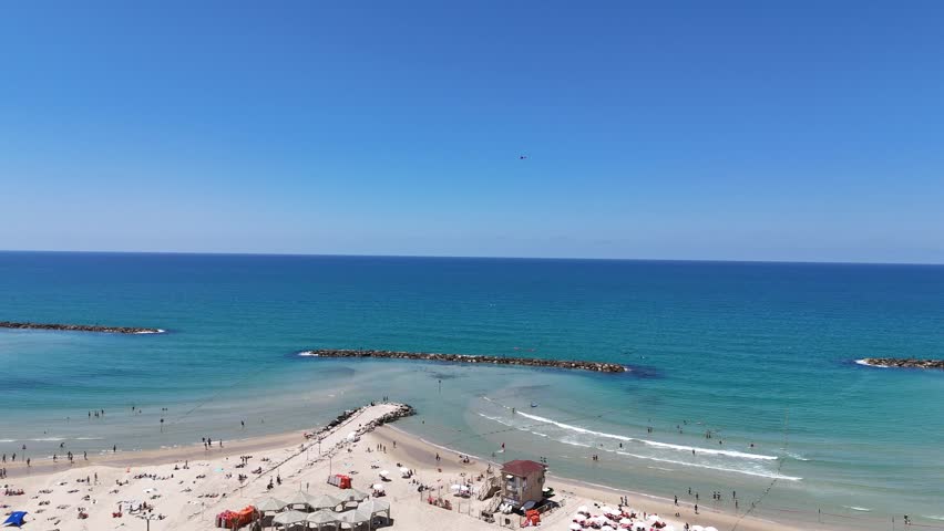 Aerial 4K view of Tel Aviv coastline, bustling promenade, luxury hotels, and sandy beach on a sunny day, Israel