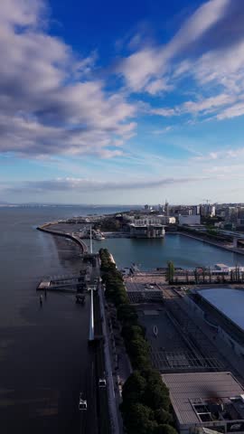 Aerial view of cable cars over Tagus river and waterfront under dramatic clouds. Lisbon, Portugal. Vertical video