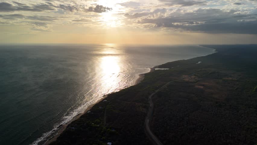 Sun setting over the ocean and shining on the water. The coastline and land are visible in the background.