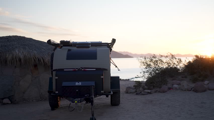 A teardrop camper trailer sits on the beach at Bahia De Los Angeles while the sun rises over the Sea of Cortez in Baja California.