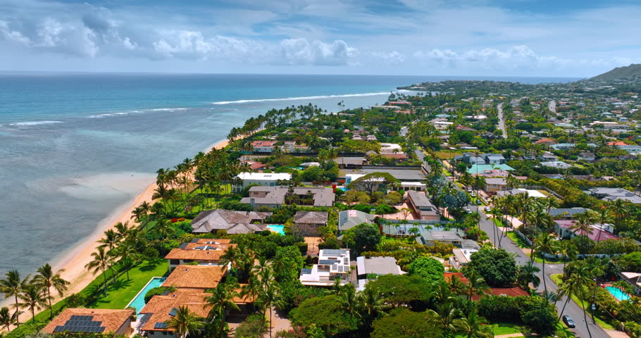 Flight over the low-rise residential area along the Pacific Ocean coast. Iconic scenery of Hawaii, USA from drone footage.