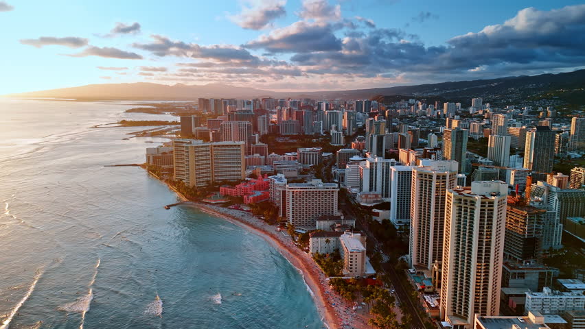 Flying over the narrow beach with multiple people on it. Aerial view of Waikiki resort at sunset. Hawaii, USA.