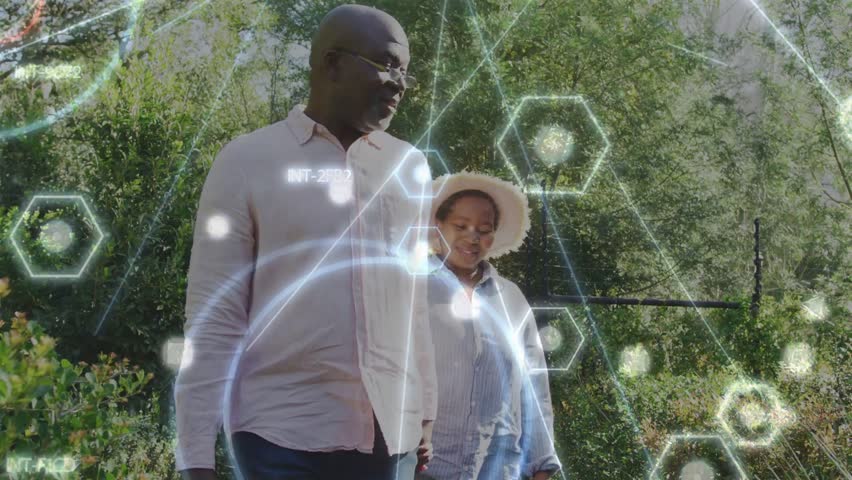 Senior couple handholding walking, man turning to woman, she conversing, tech holograms overlaying. Garden, park, outdoor, pair, affection, sunlit, greenery